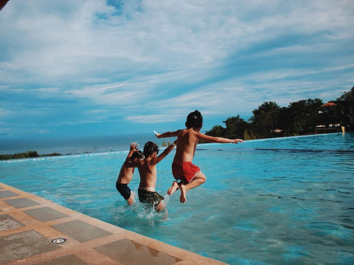 three kids jumping into the pool together