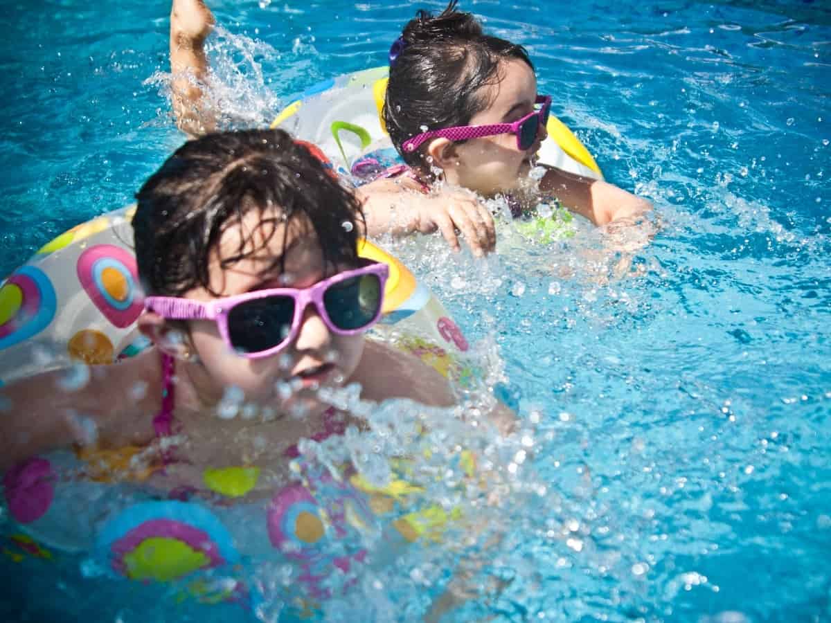 two young girls with sunglasses on in the pool practicing pool safety