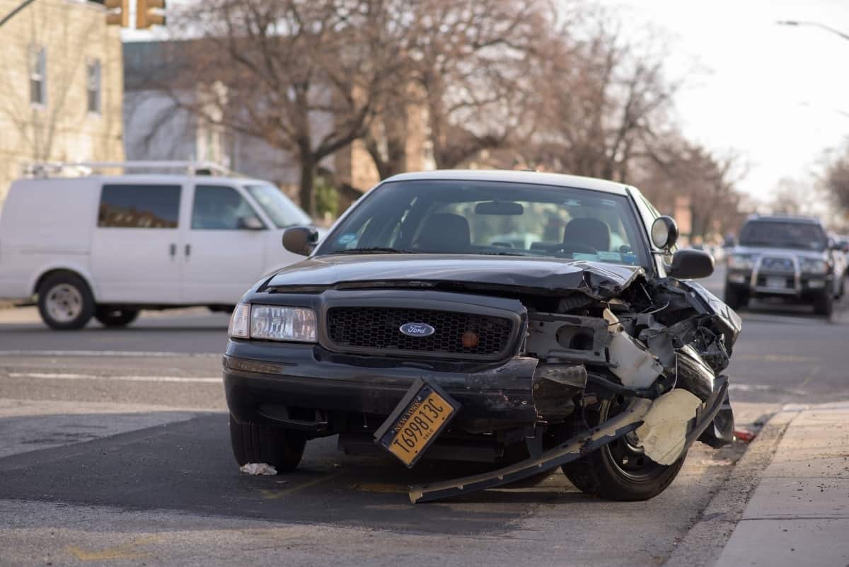A black car with damage on the driver's side is parked on a road.