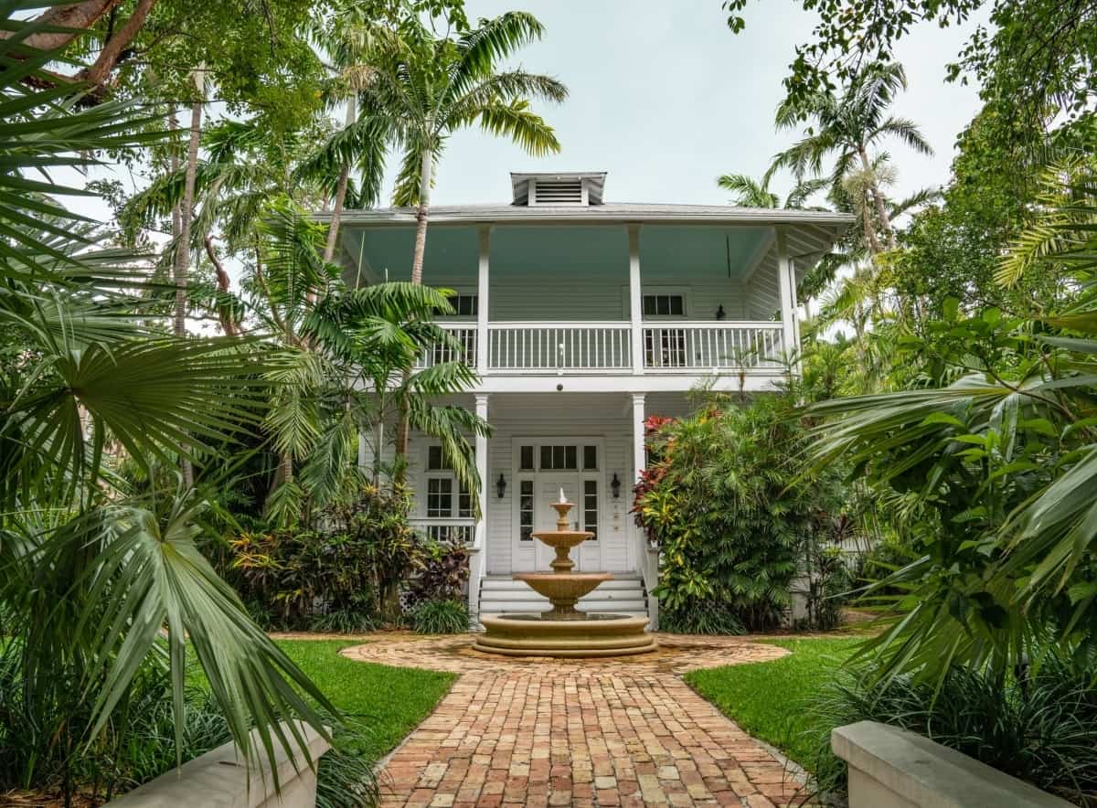 A vacation home in Key West Florida is surrounded by palm trees and other tropical green landscaping.