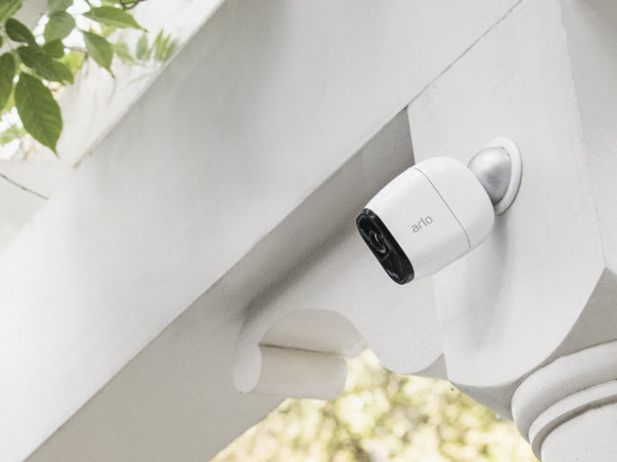 an arlo security camera mounted on a house with flowers