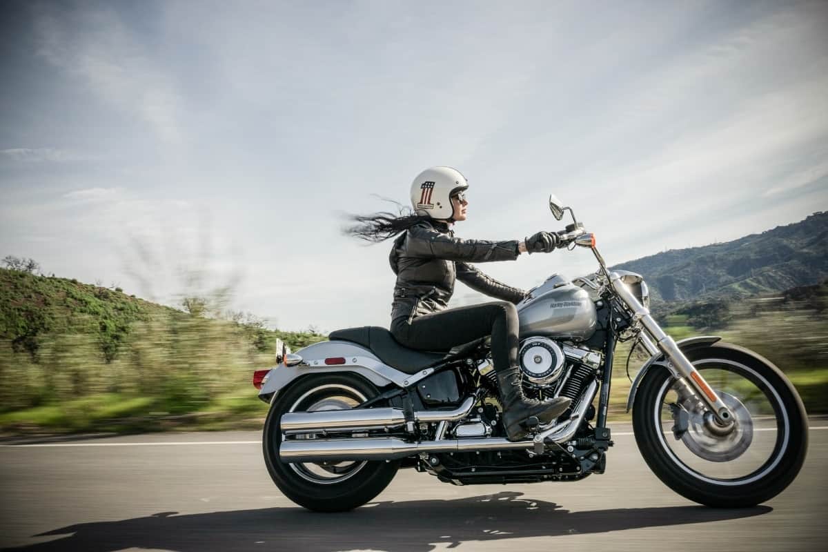 A woman wearing a leather jacket is driving a motorcycle down a road.