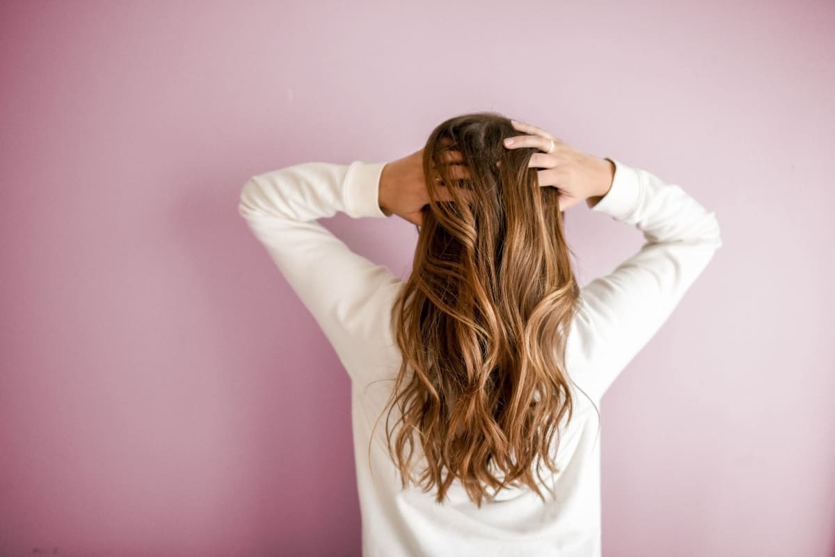 A woman facing a pink wall has long brown hair.