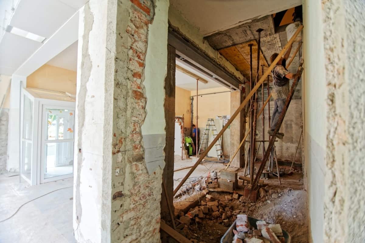 A man stands on a ladder inside of a home that's getting renovations.