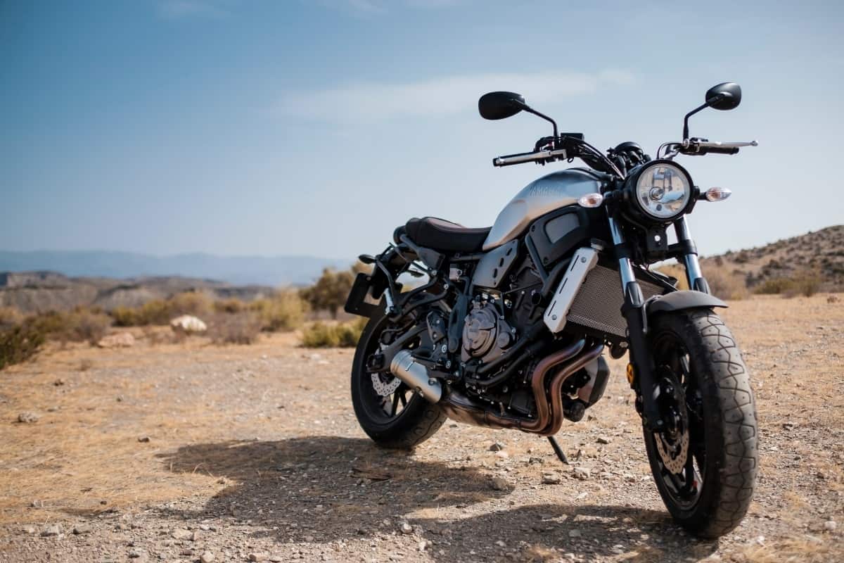 A silver motorcycle is parked on a dirt road by the ocean.