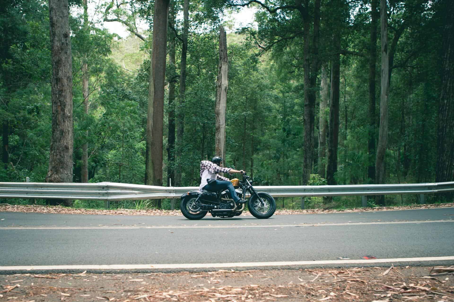 A man drives a motorcycle down a road past trees in a wooded area.