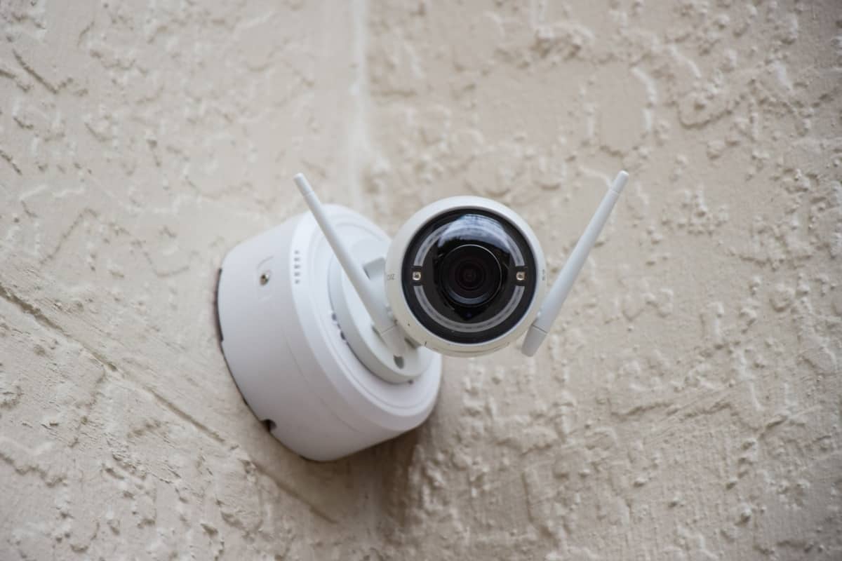 A white video surveillance camera is installed outside on a beige wall.
