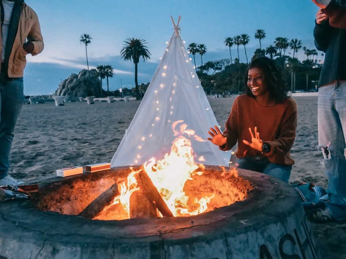 a firepit on a beach with people warming their hands around it