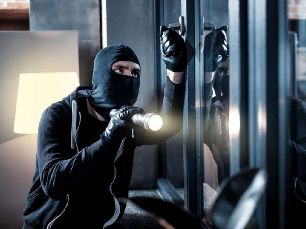 a burglar or thief breaking into a home through the door as a home invasion