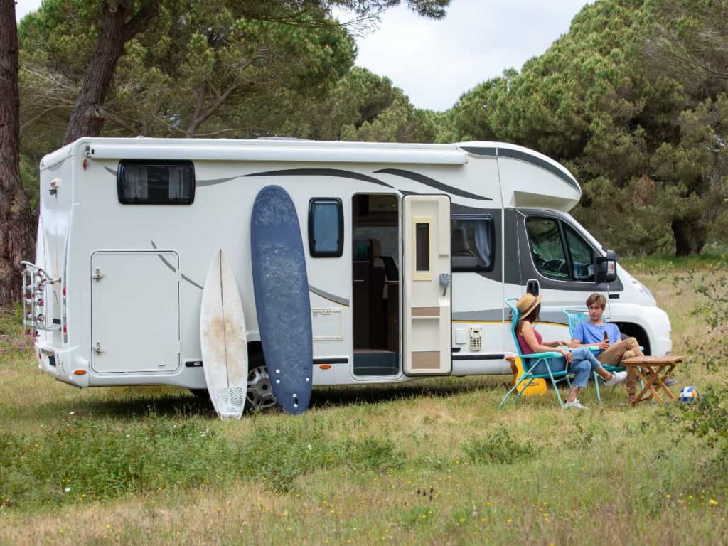 a couple sitting outside of their travel trailer with two surfboards