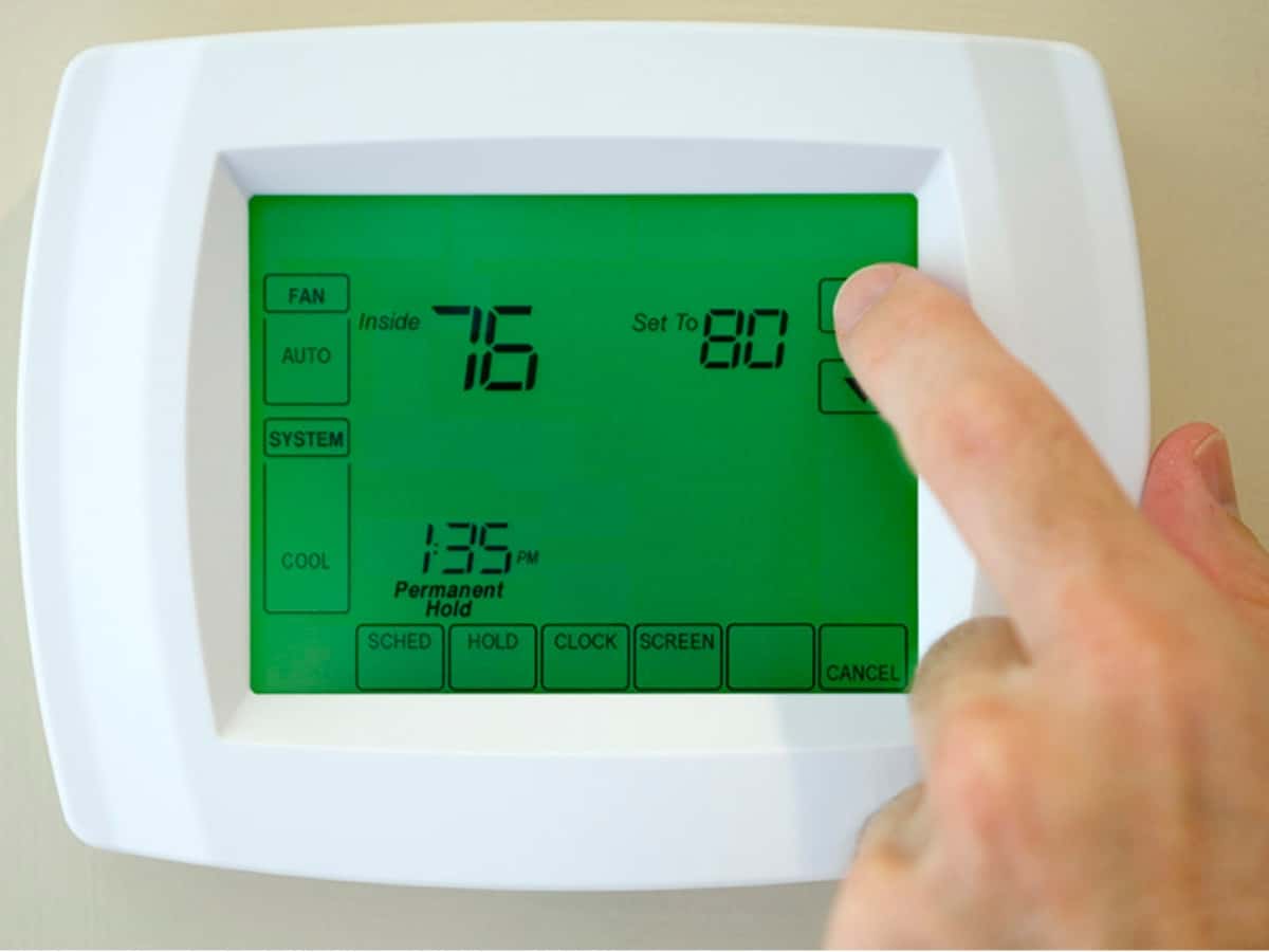 a close up of a honeywell smart thermostat with a hand adjusting the temperature