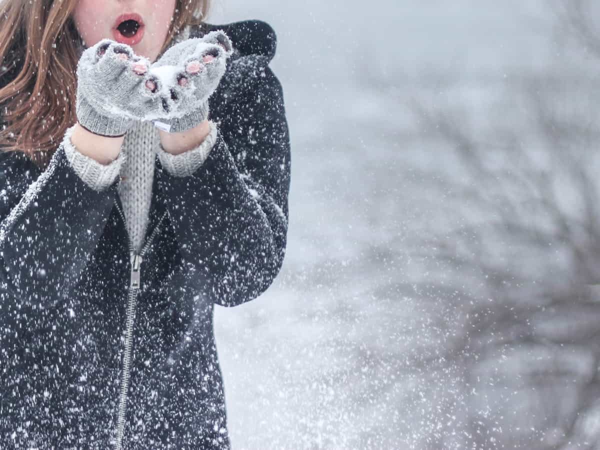 close up of woman wearing gloves and blowing snow out of her hands in the winter