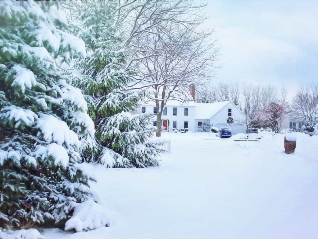 a white house surrounded by trees and snow during winter