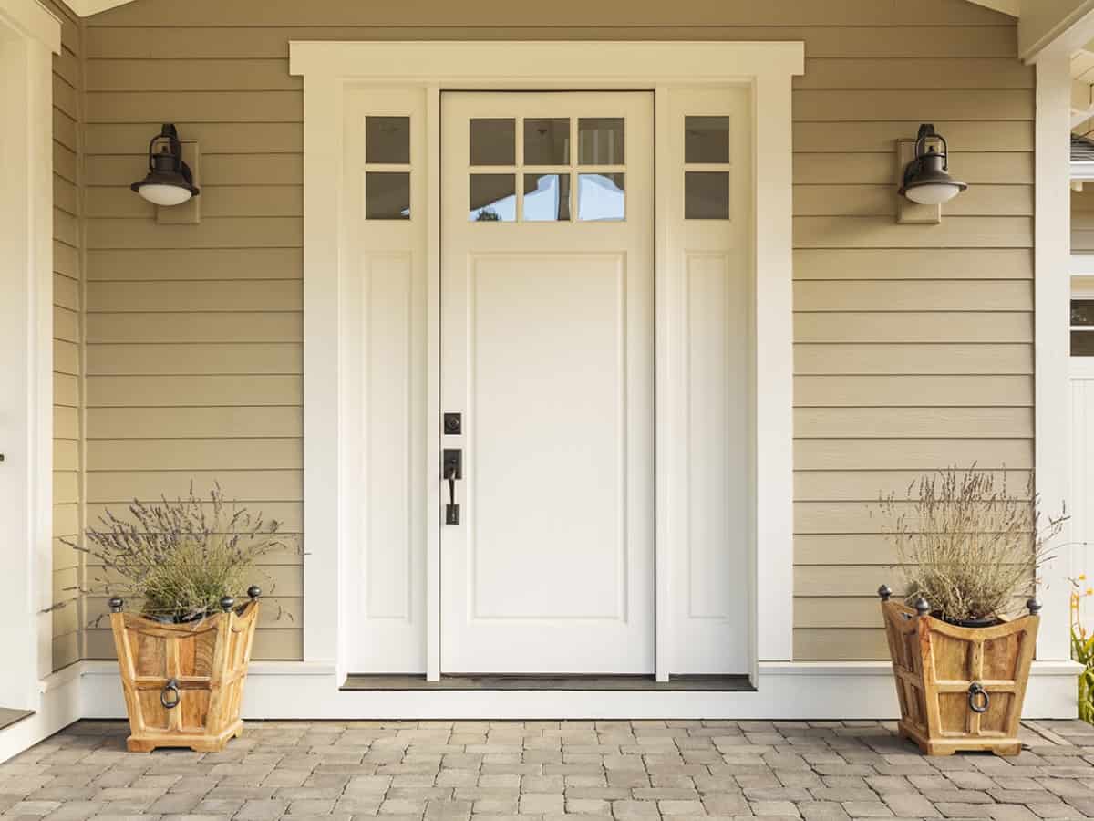 White front door with small square decorative windows and flower pots