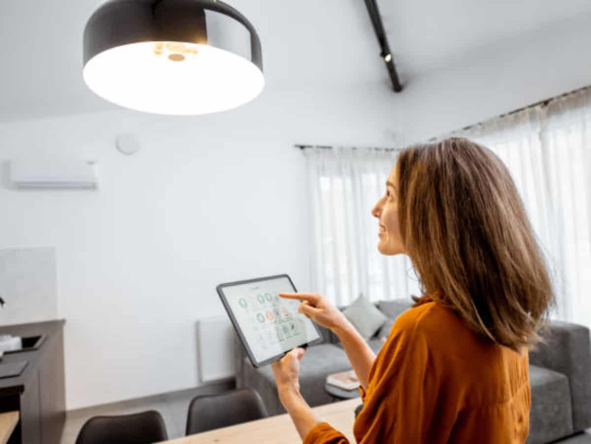 Young woman controlling home light with a digital tablet in the living room. Concept of a smart home and light control with mobile device