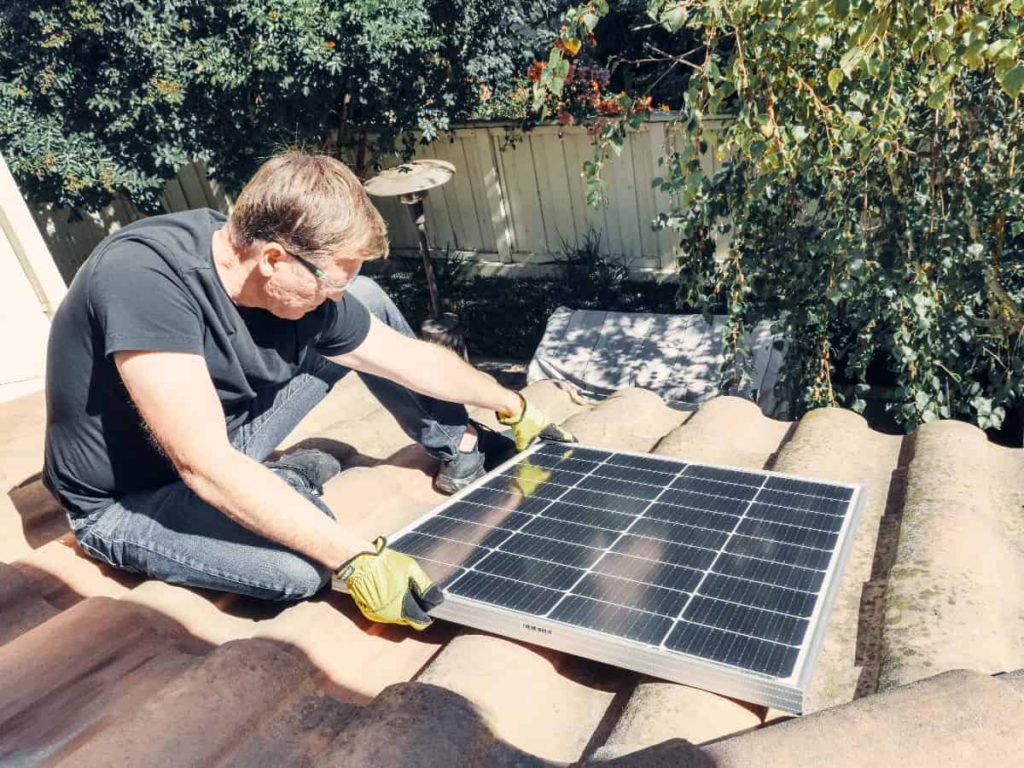 a man on a roof installing a solar panel for renewable energy