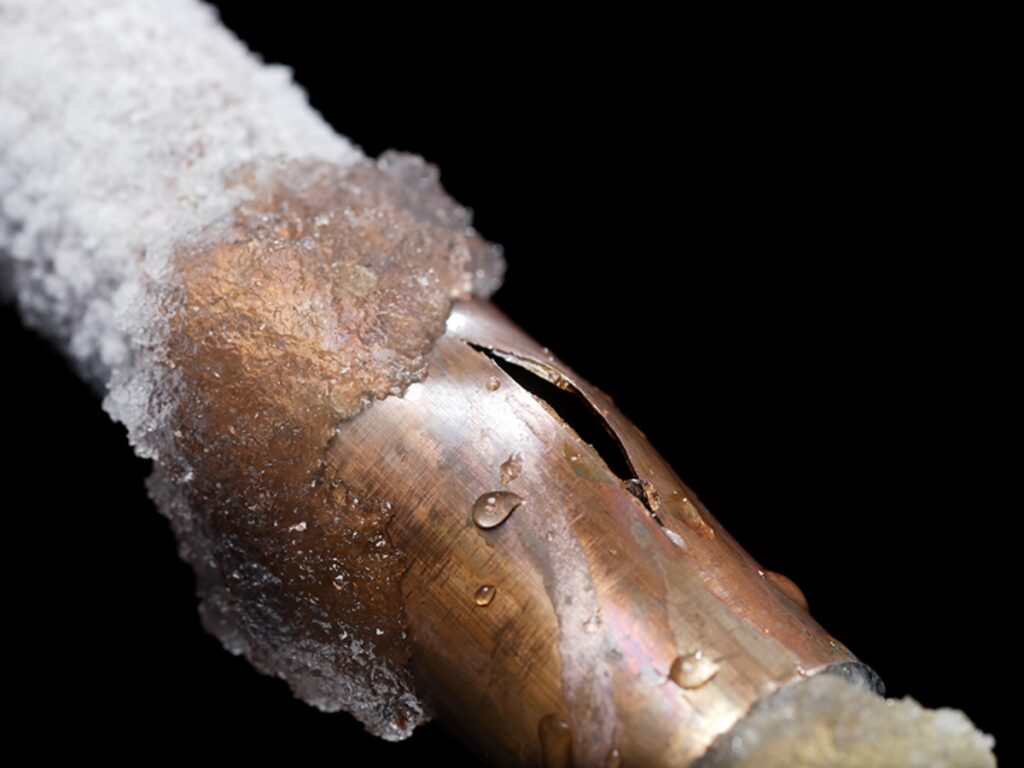 an upclose image of a frozen and burst pipe with snow on it