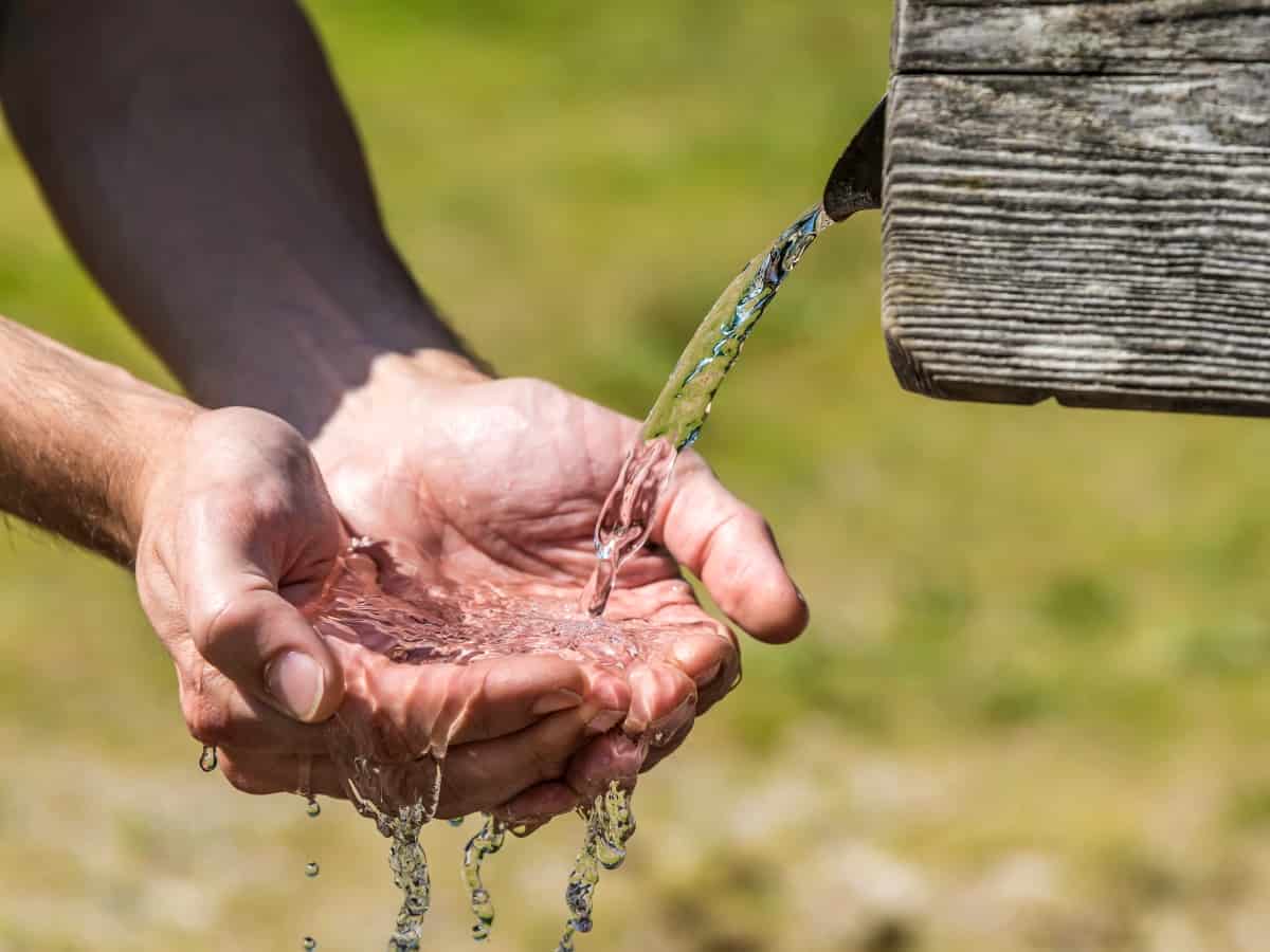 hands reaching under well water for fresh water