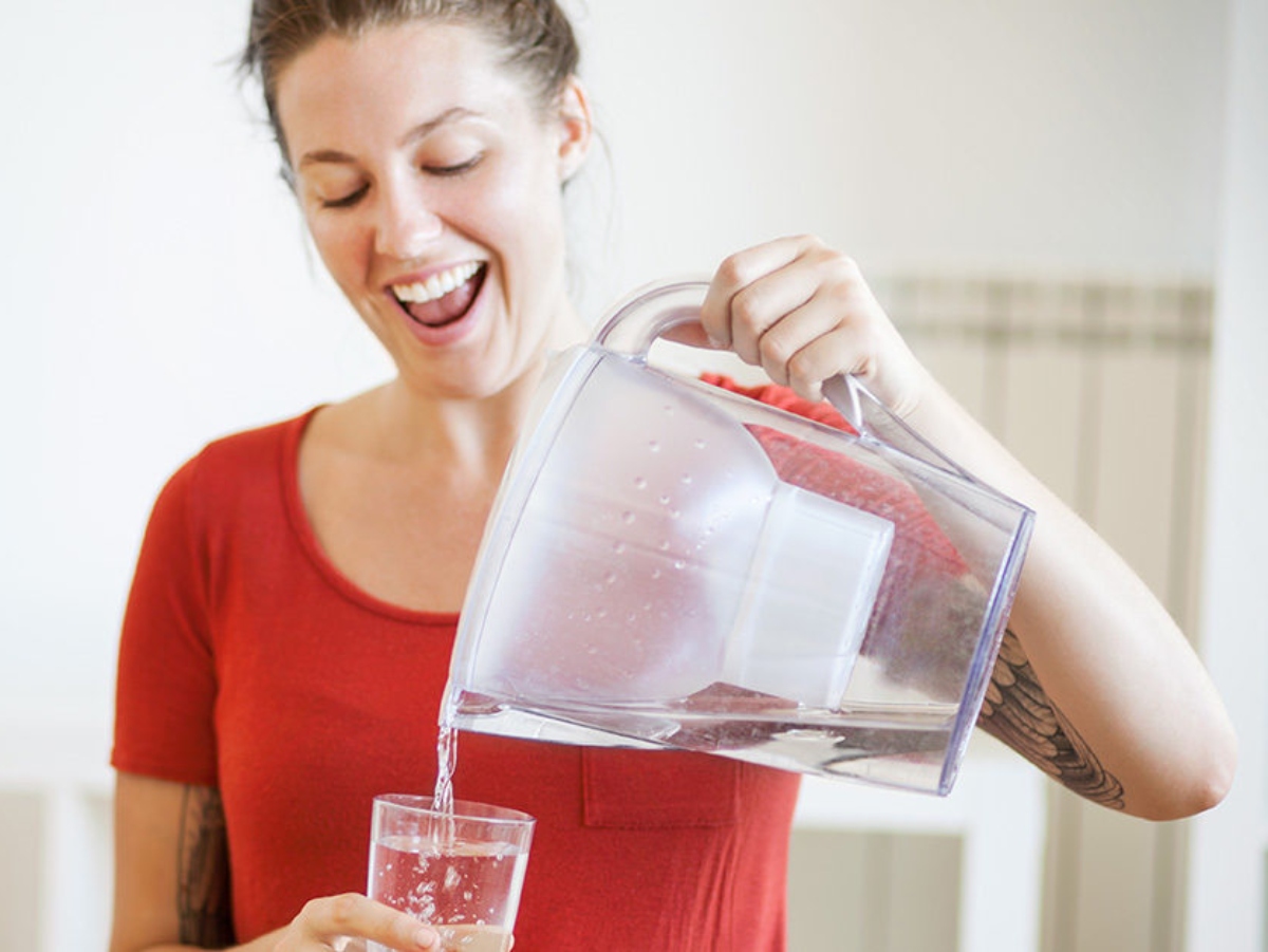 a woman holding a brita pitcher and pouring the water into a glass