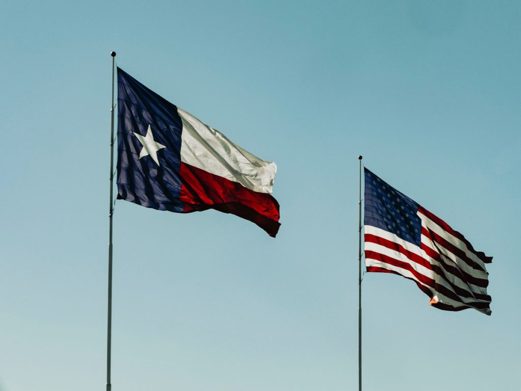 a texas and american flag against a blue sky
