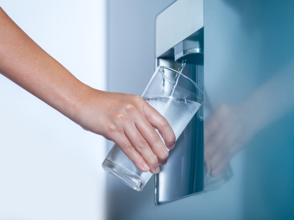 someone filling up a cup of water from a refrigerator with a fridge filter