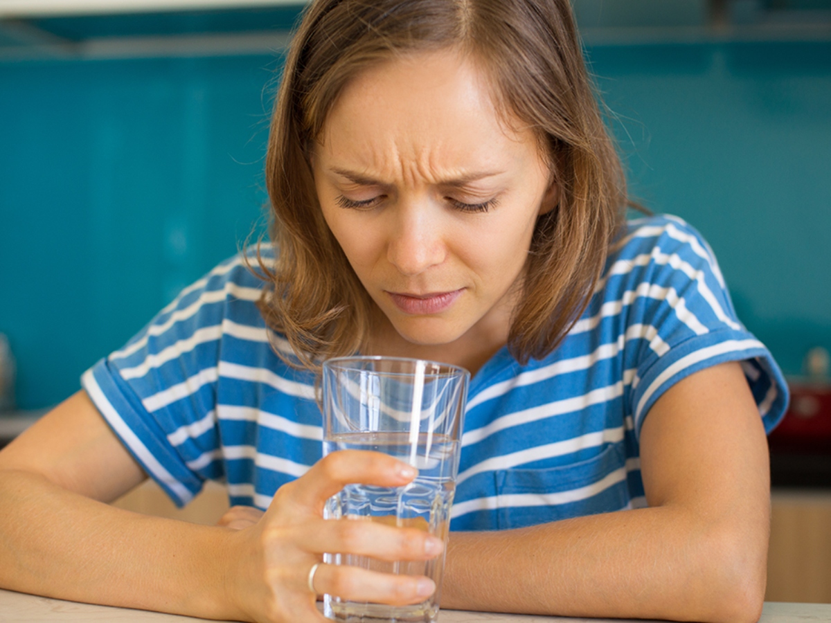 a woman close to her water cup wondering why her well water smells