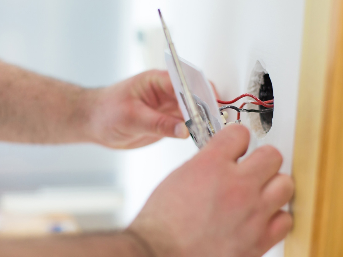 someone placing an outlet back into the wall for home wiring