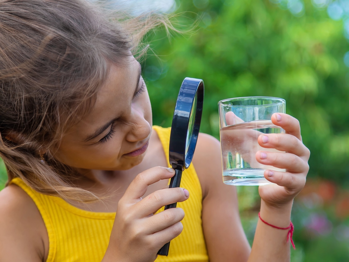 a little girl holding up a magnifying glass to a cup of water to look for contaminants