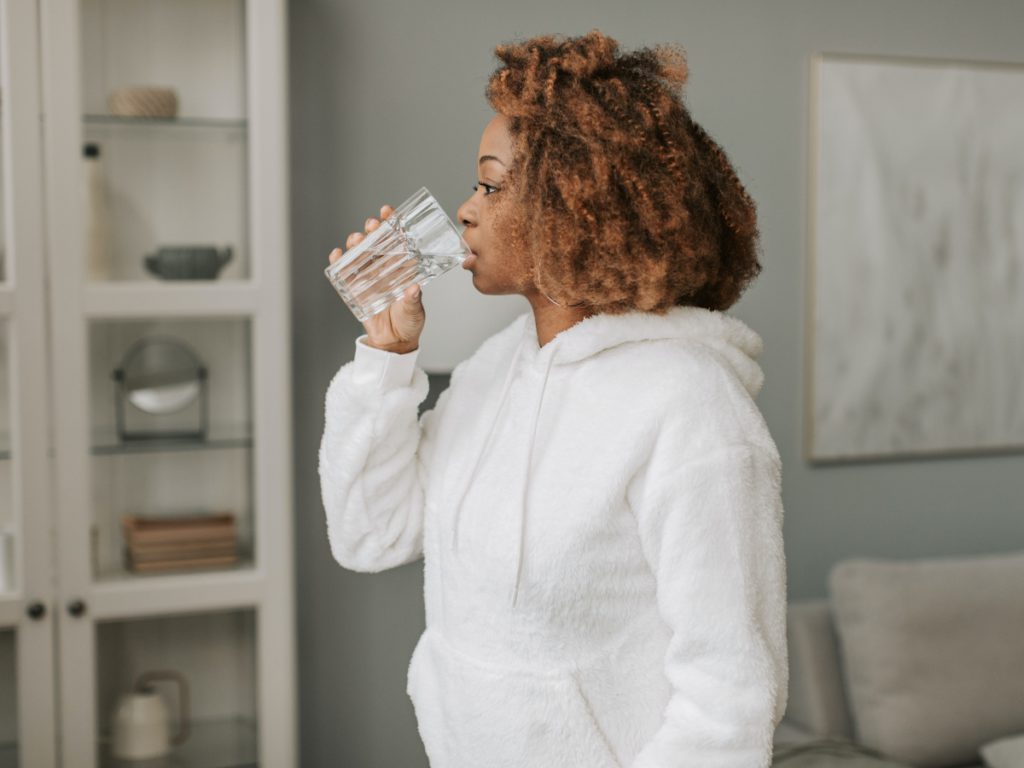 a woman in a white sweatshirt drinking water straight from a glass