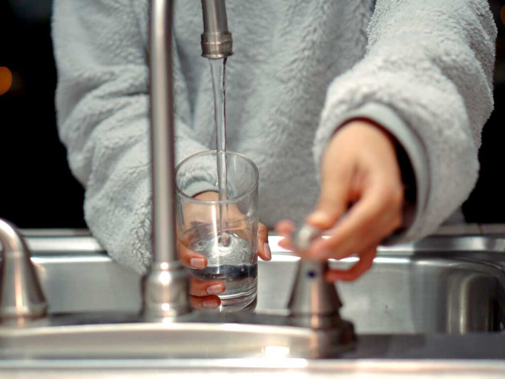 a woman standing in front of a sink letting water out of the faucet into a glass
