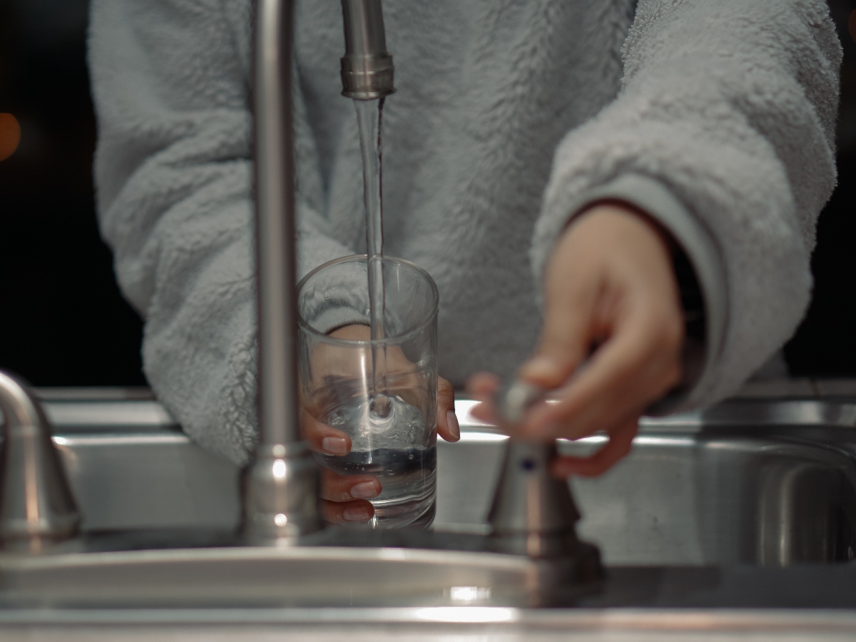 a person filling up a water glass at the sink