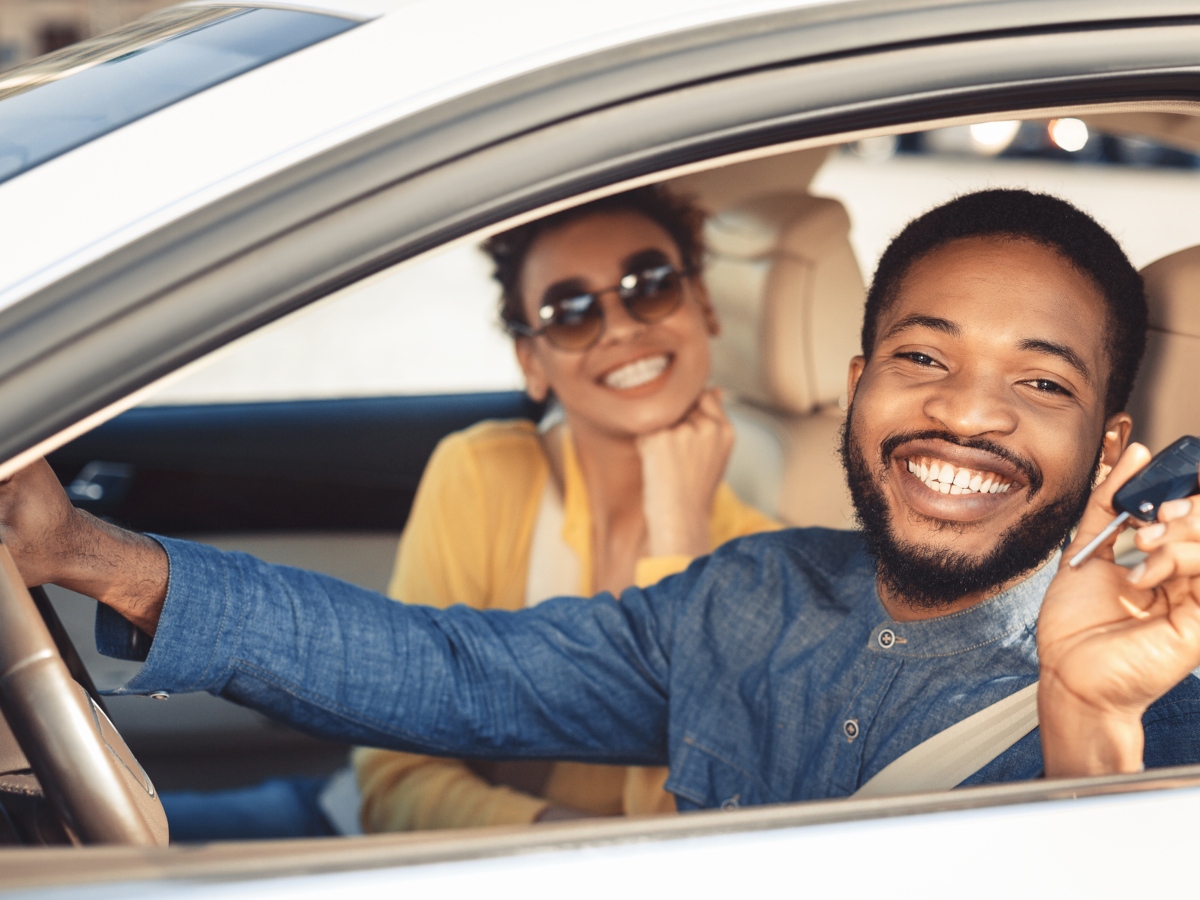 two young people sitting in a car with the man's hand on the steering wheel
