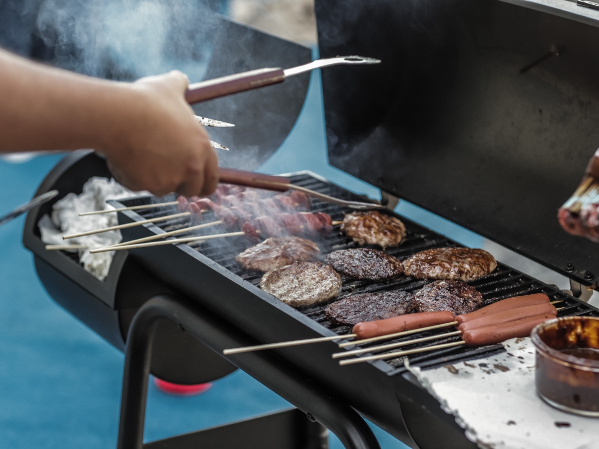 a pair of hands holding tongs flipping burgers and hotdogs on a grill 