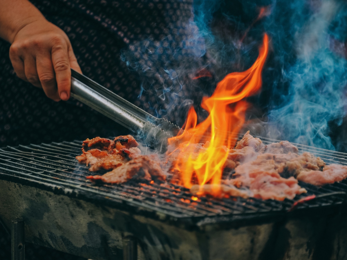 a hand flipping a burger on the grill with an open flame or fire