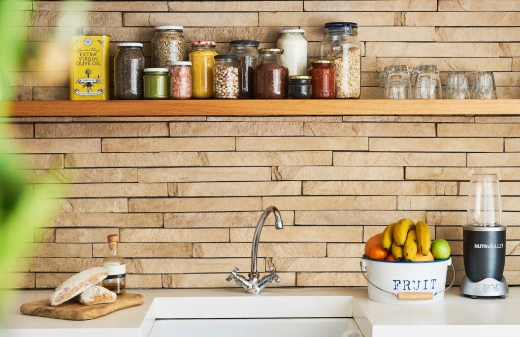 A kitchen sink beneath a shelf of glass jars filled with oats, seeds, and different nuts.