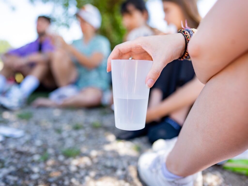 a hand holding a plastic cup of water outside with a group of people