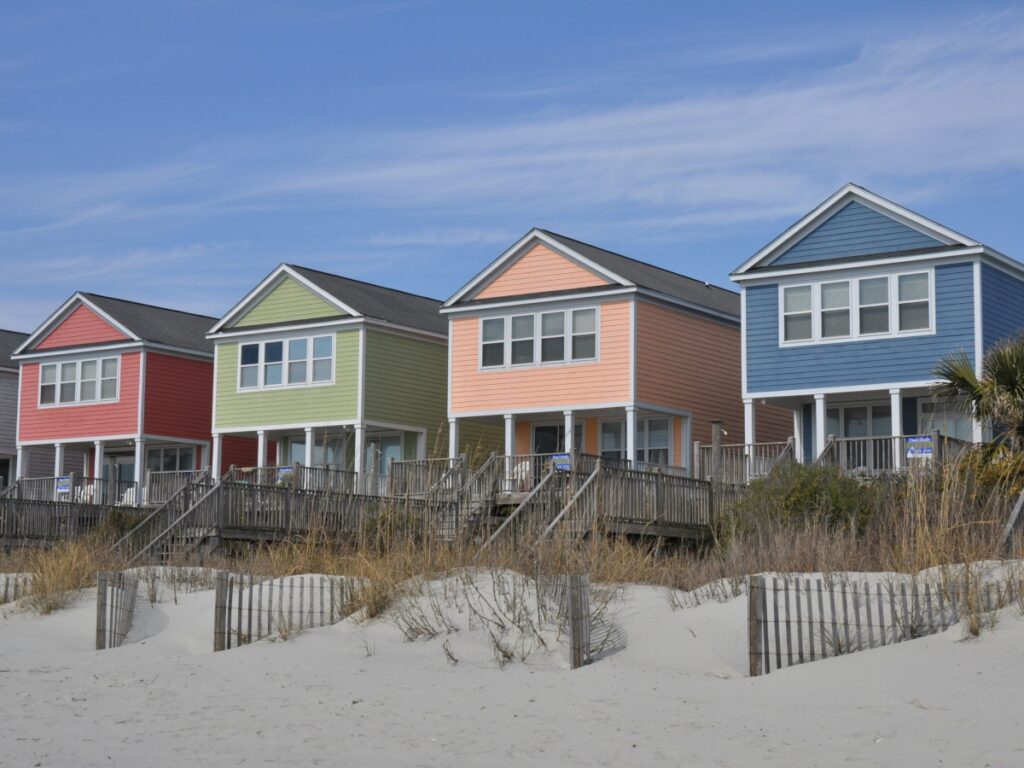 a row of four vacation homes alon gthe beach, a red house, green house, orange house and blue house