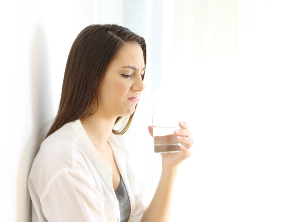 a woman leaning against a white wall looking into a glass of water