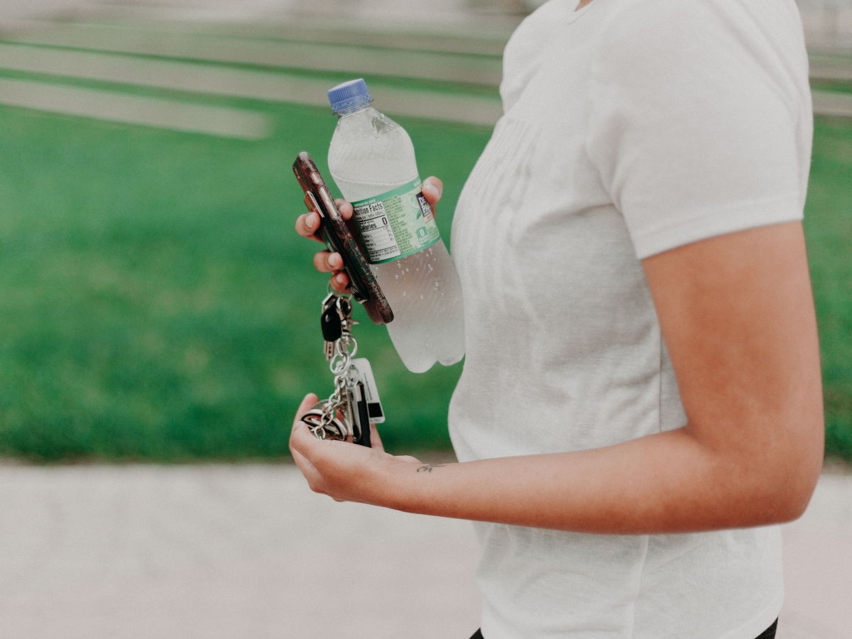 a person in a white shirt holding water bottle and car keys outside