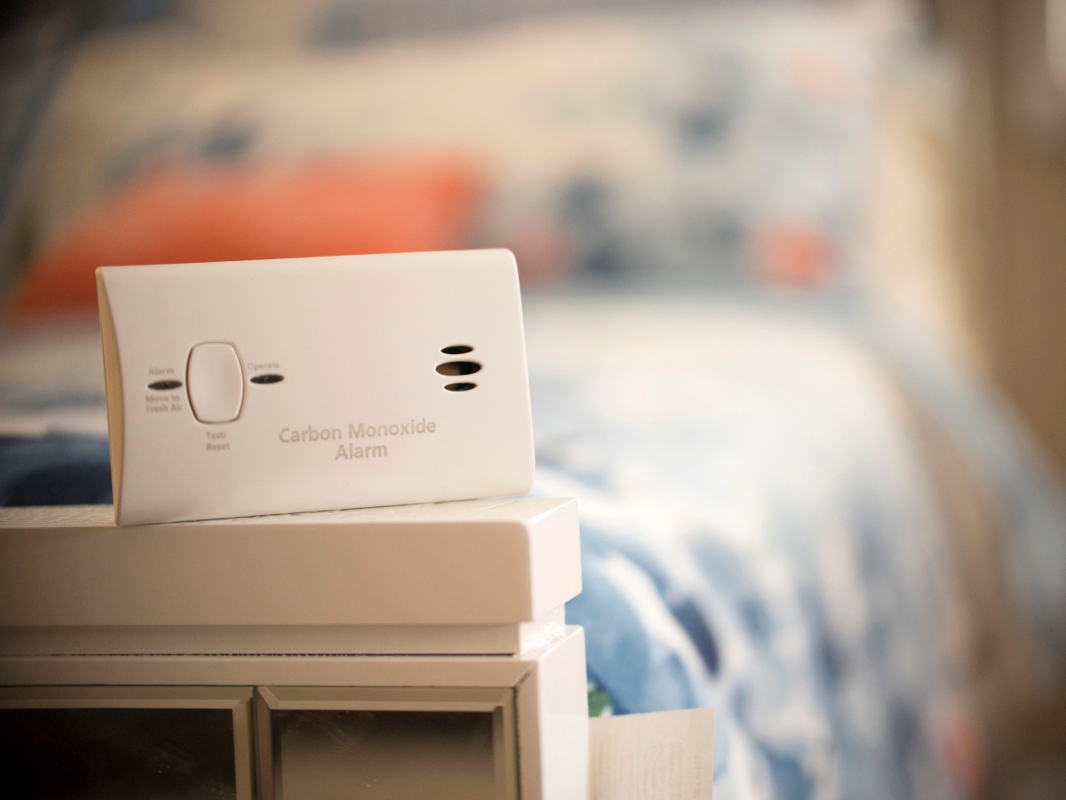 a carbon monoxide alarm sitting next to a bed in a bedroom