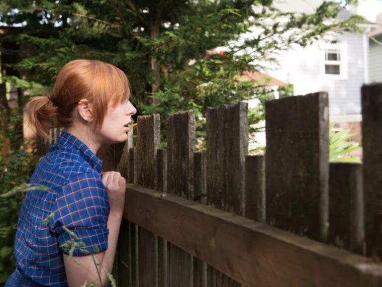 woman leaning against fence looking at neighbors