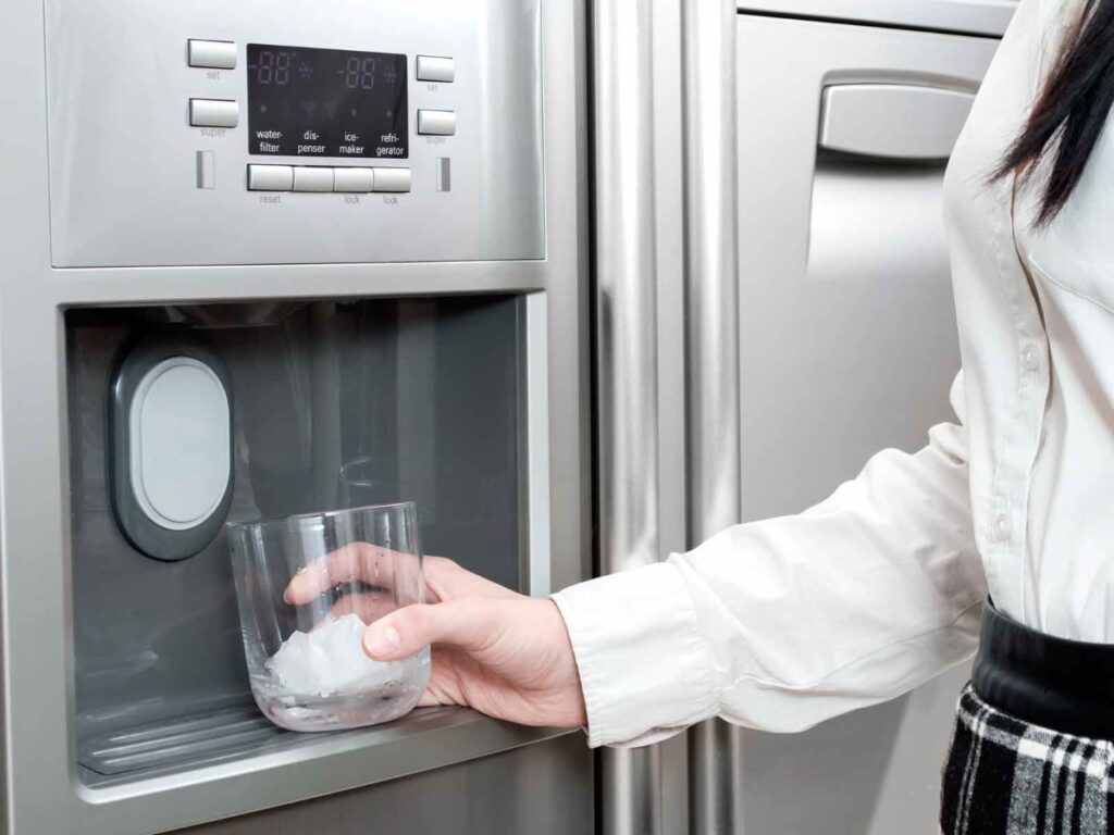 a woman with a glass against a refrigerator getting ice from the fridge